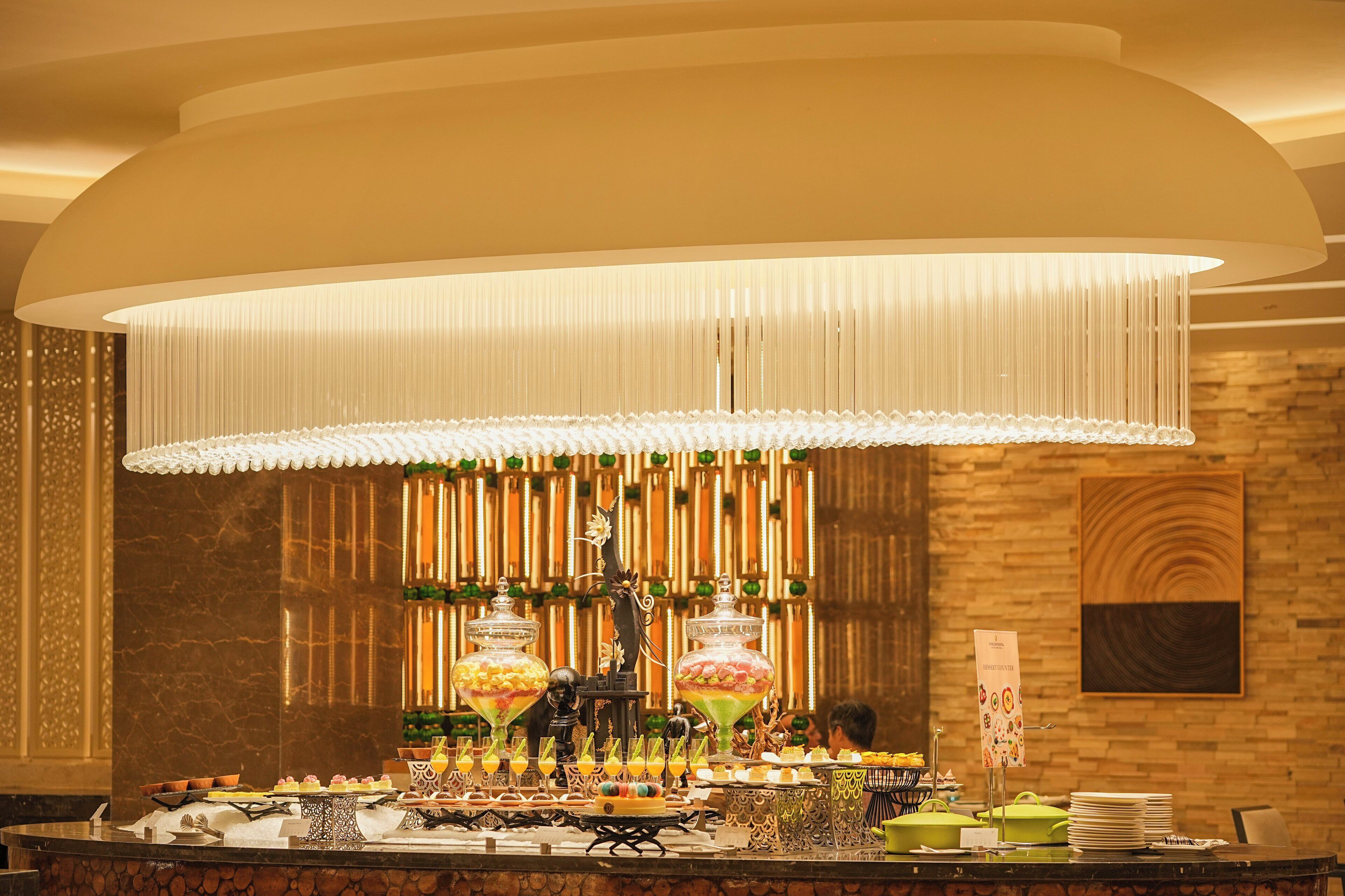 A buffet setup with various food items and a large hanging light fixture.