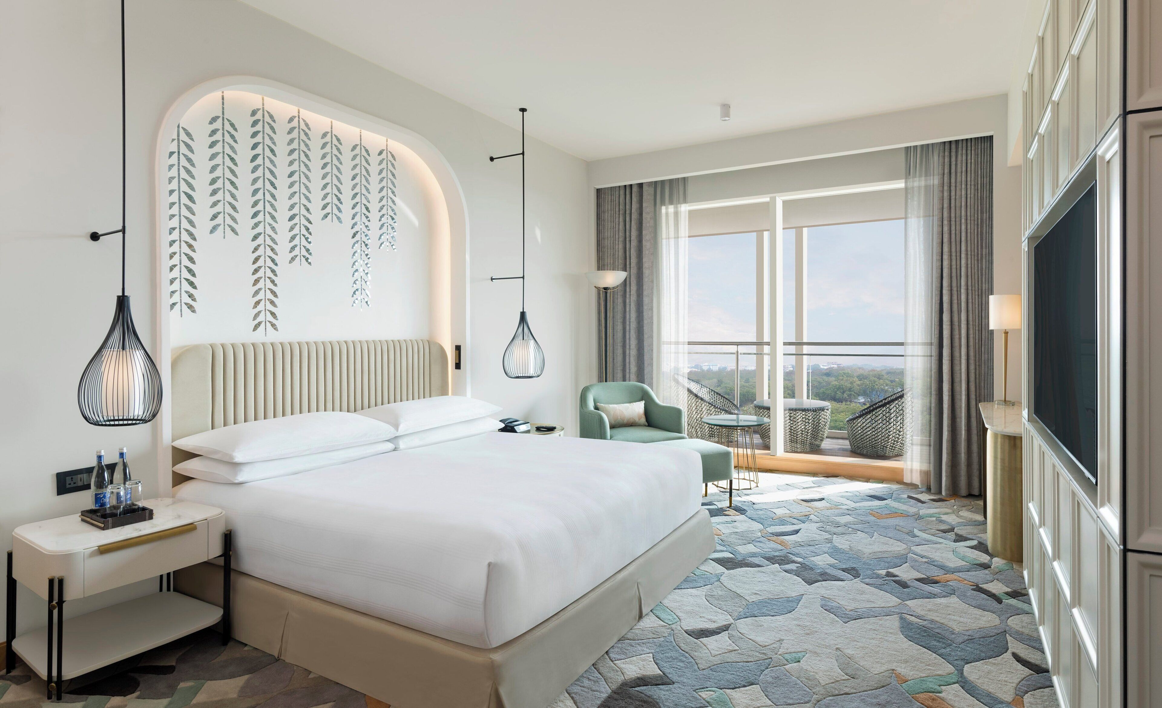 A hotel room with a large bed, a bedside table, a chair, a balcony with a view, and a TV.