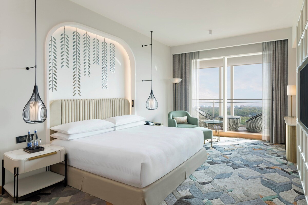 Ein modernes Hotelzimmer mit einem großen Bett, einem Schreibtisch, einem Stuhl und einem Balkon mit Blick.
