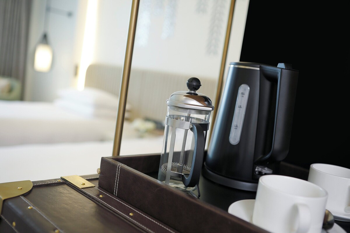 Ein Kaffeeautomat, eine Glascarafe und zwei weiße Tassen auf einem Tablett in einem Hotelzimmer.