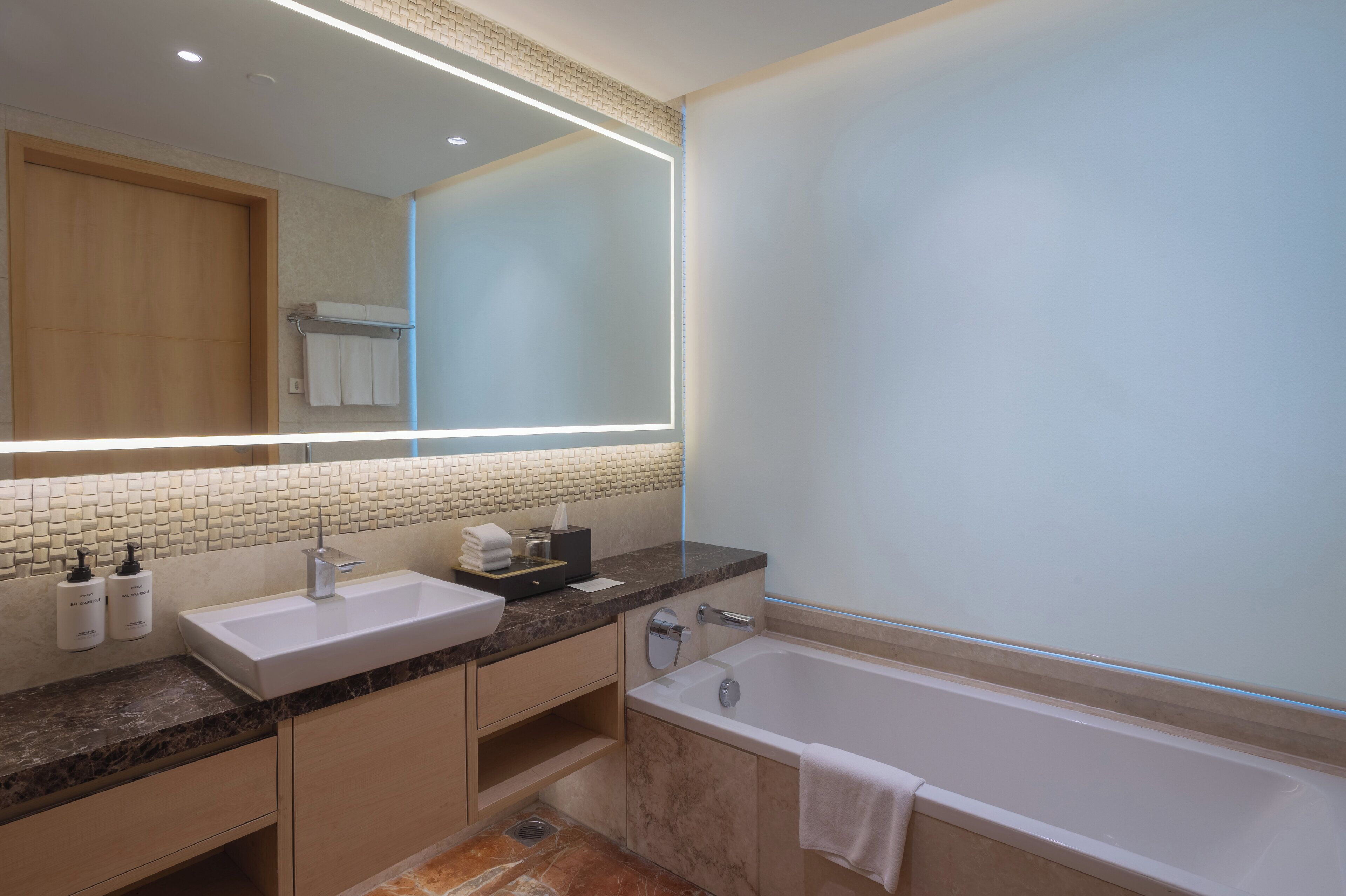 A modern bathroom with a large mirror, a sink, a bathtub, and a vanity with a towel rack.