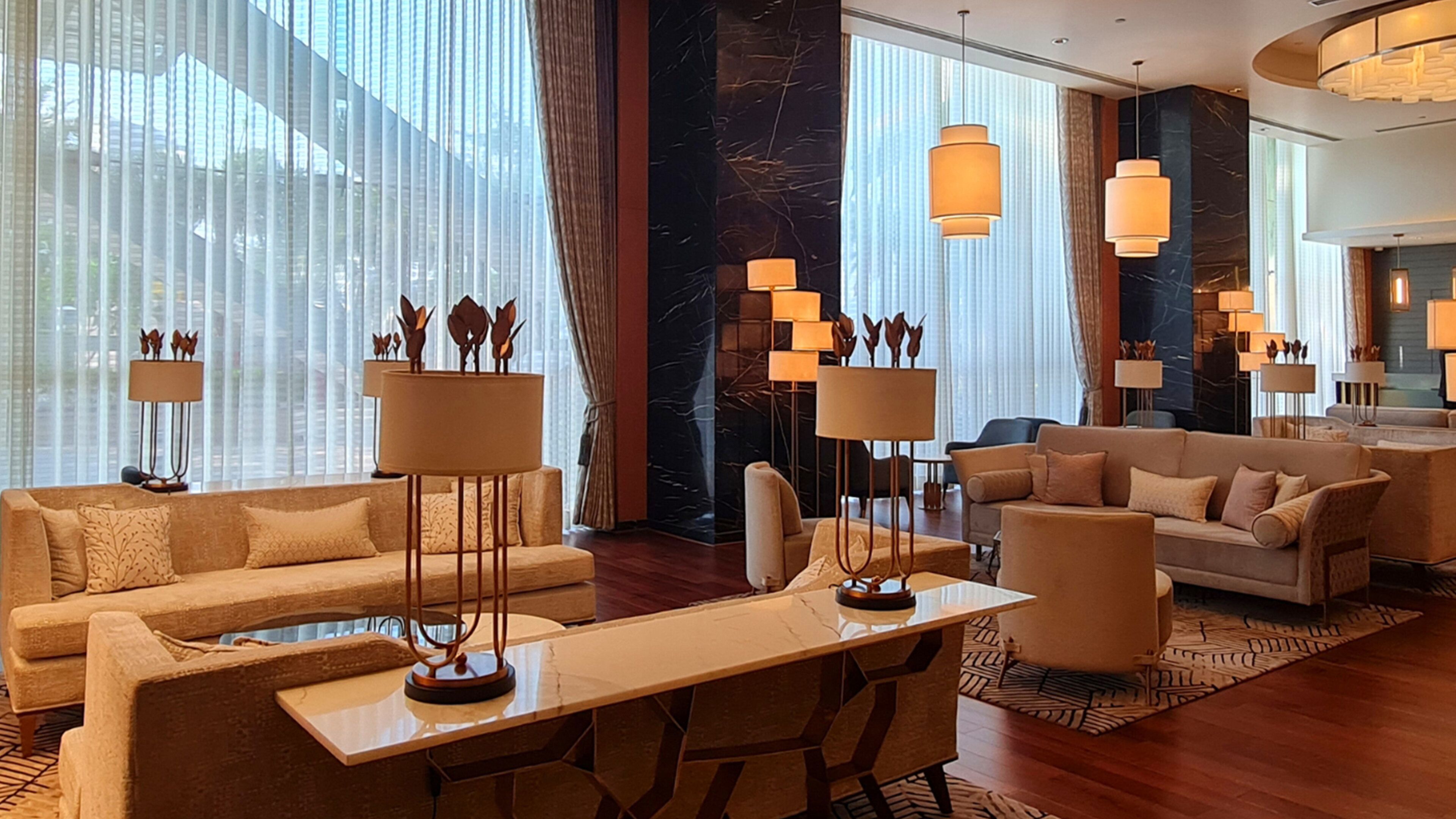 A modern hotel lobby with a large seating area, multiple lamps, and a marble accent wall.