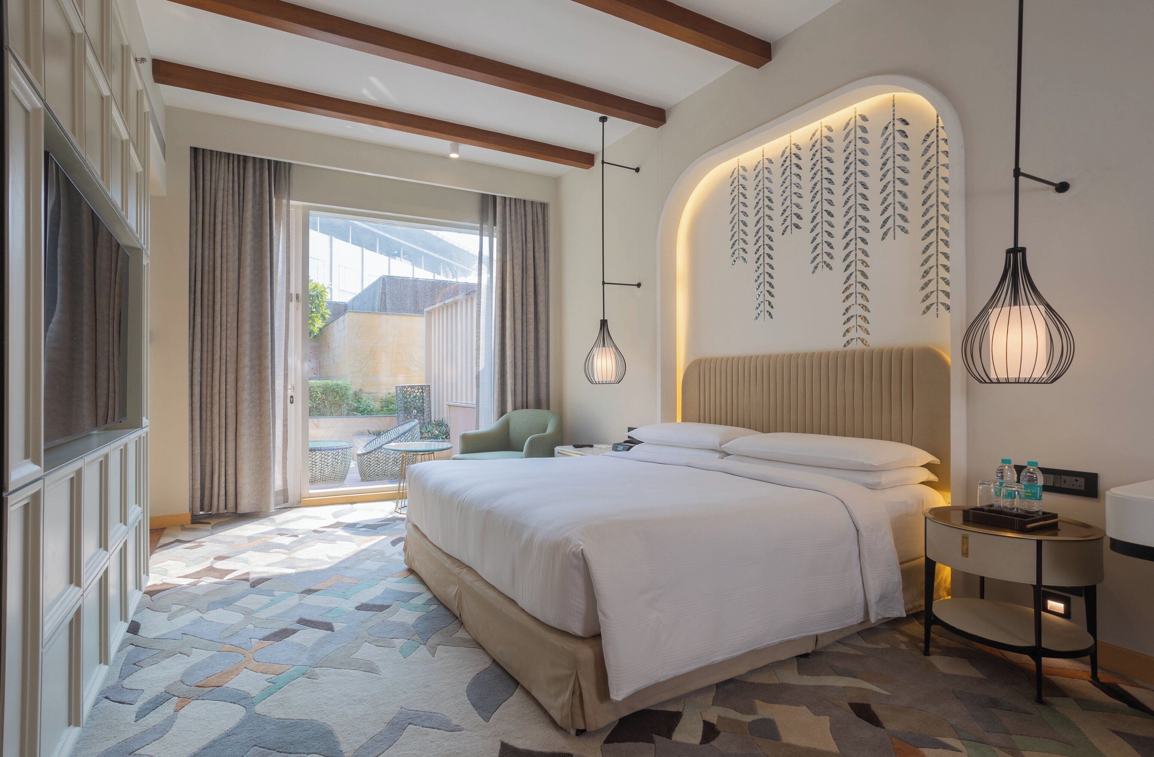 A modern hotel room with a large bed, a small table, and a view of the outdoors.