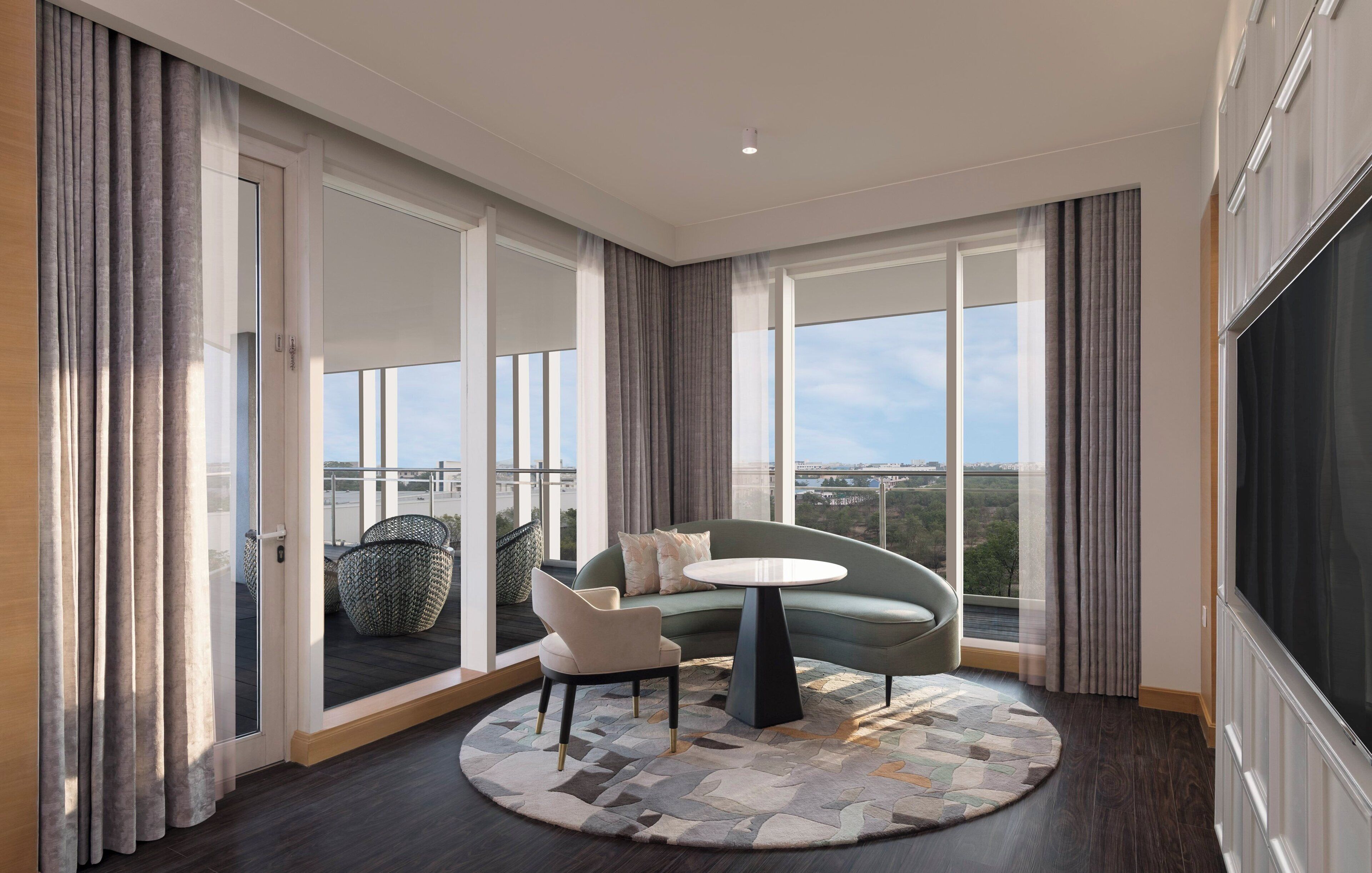 A modern living room with a round table, two chairs, a sofa, and a view of a cityscape through large windows.