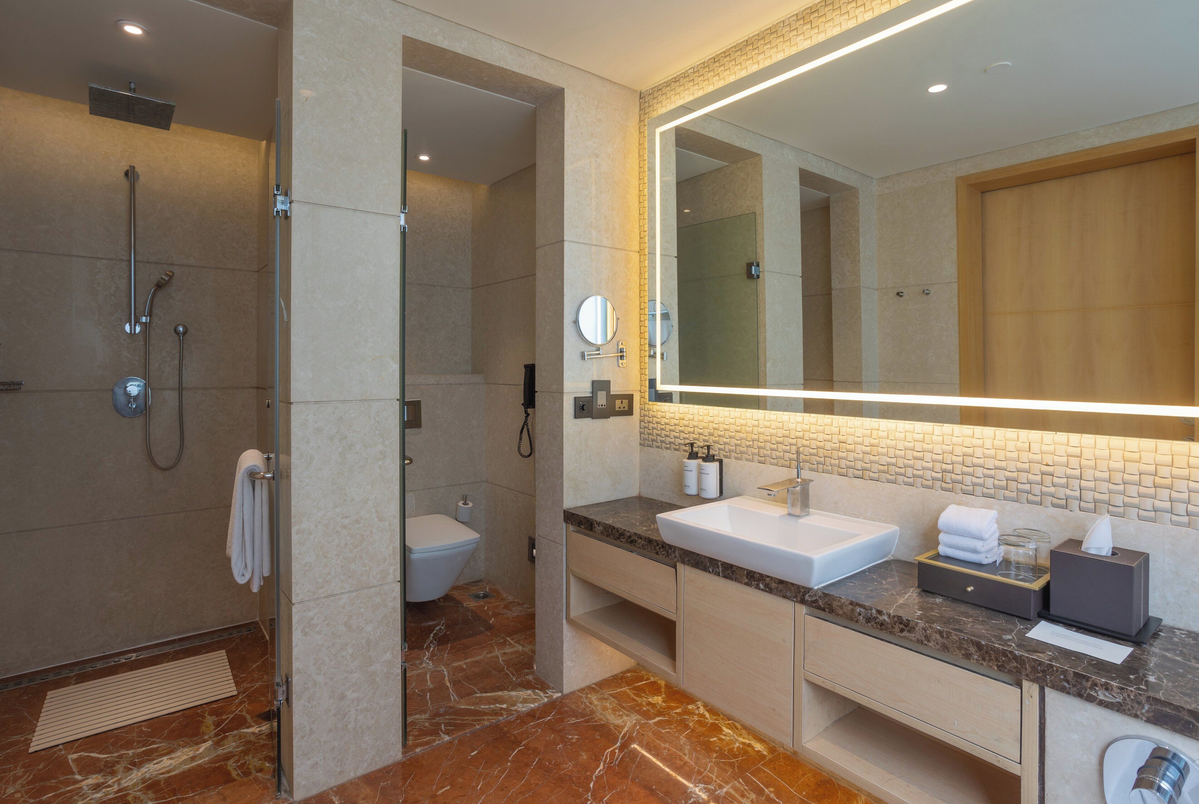 A modern bathroom with a shower, toilet, and vanity with a large mirror and marble flooring.