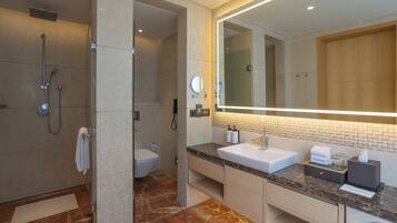 A modern bathroom with a shower, toilet, and vanity with a large mirror and marble flooring.