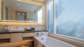 Une salle de bain moderne avec un grand miroir, deux lavabos, une baignoire et une fenêtre donnant sur un paysage agréable.