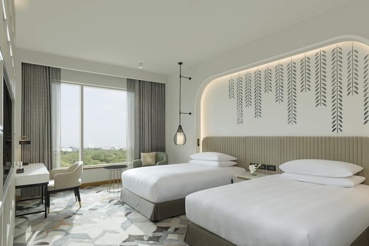 Een moderne hotelkamer met twee bedden, een bureau en een groot raam met uitzicht op de stad.