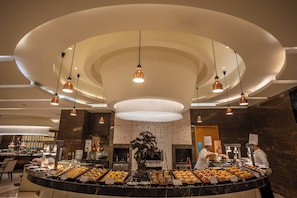 Un espace buffet doté d’un îlot central, d’un éclairage suspendu et d’un mur en marbre.