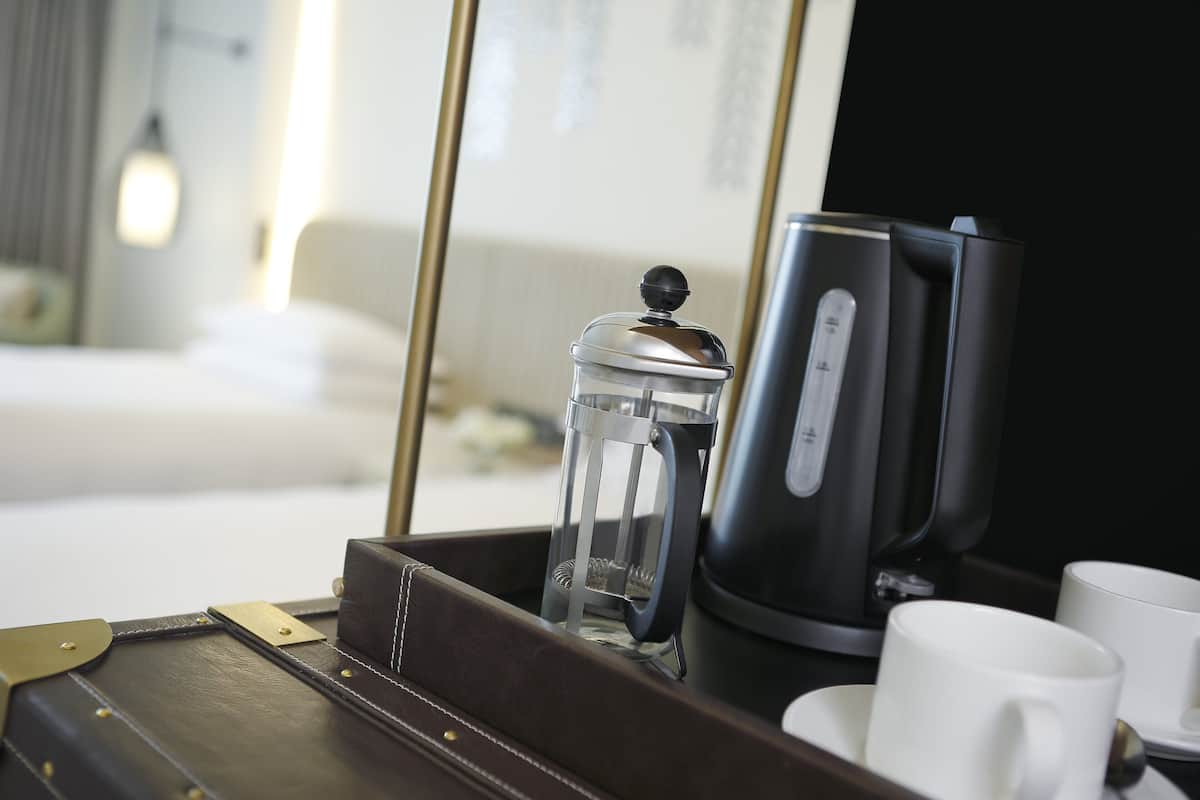Een koffiezetapparaat, een glazen kan en twee witte kopjes op een dienblad in een hotelkamer.