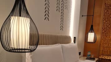 A hotel room with a bed, a bedside table with a phone and a digital clock, a hanging pendant light, and decorative wall art.