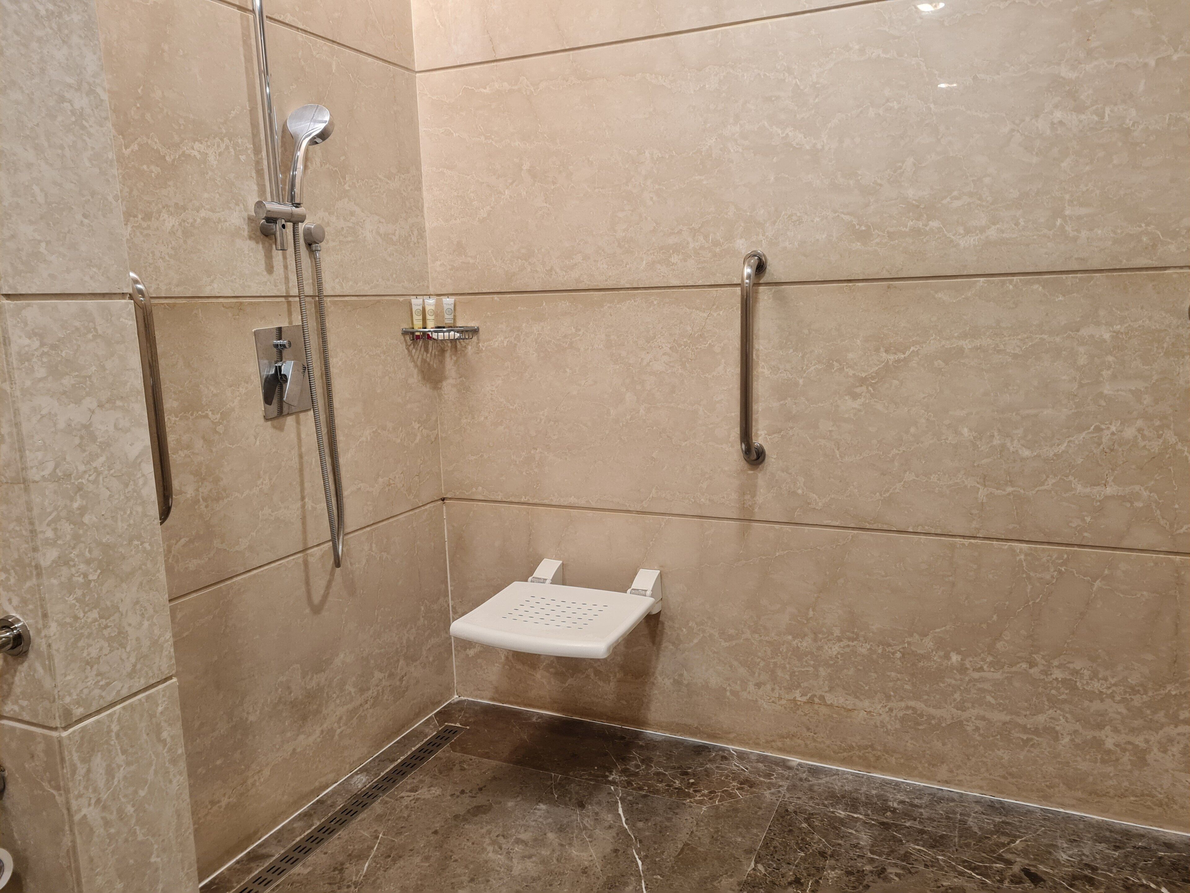 A shower area with a handheld showerhead, a wall-mounted faucet, and a shelf with toiletries.