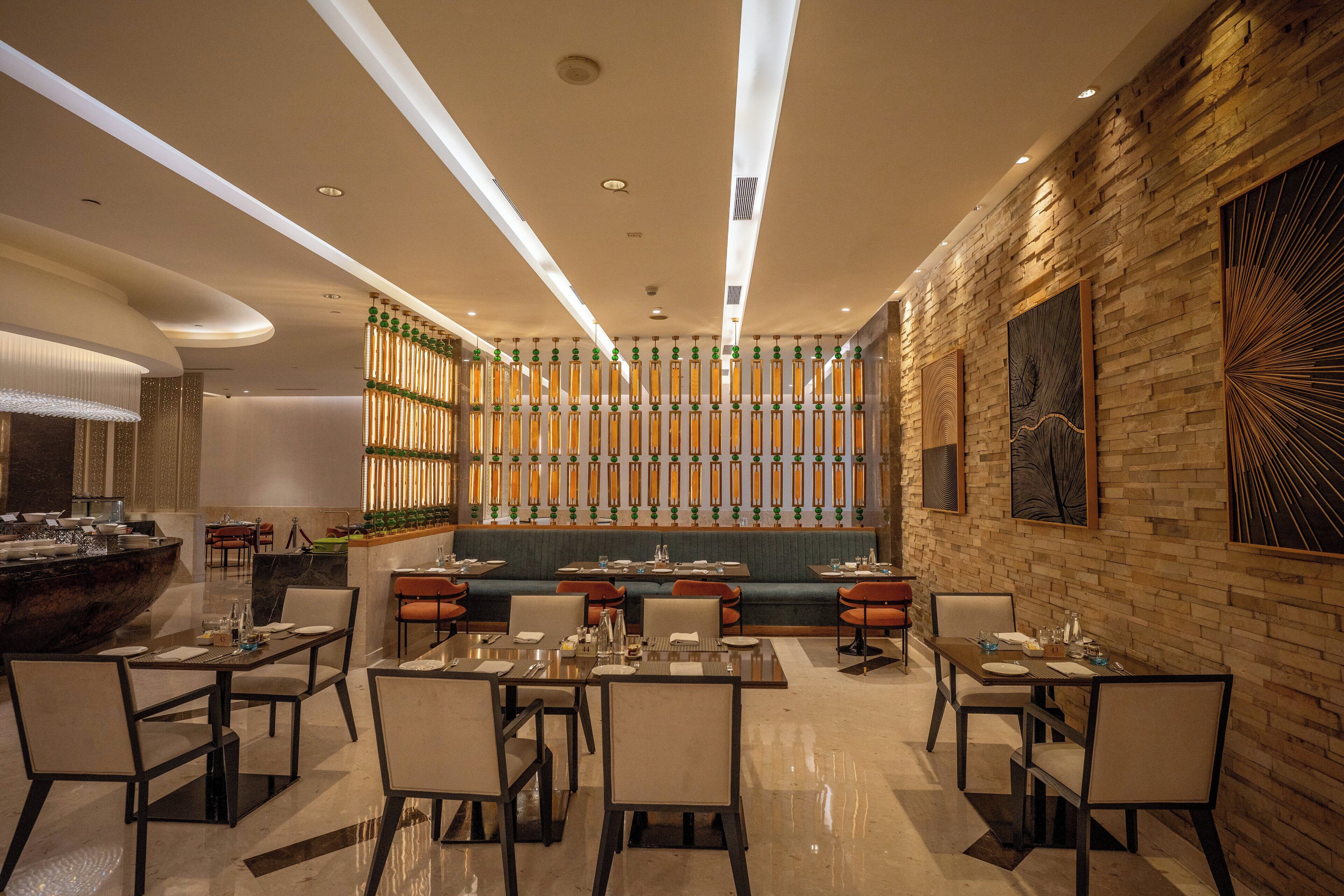 Een modern restaurant met een centrale zithoek, meerdere eettafels en een decoratieve wand met verticale elementen.