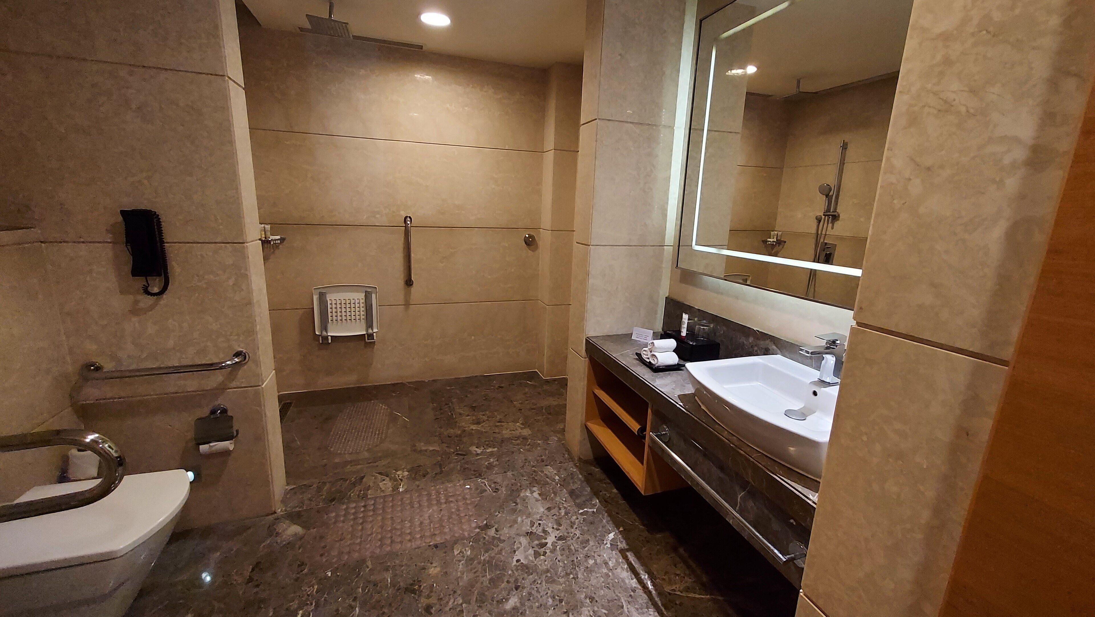 A modern bathroom with a toilet, a shower, a sink, and a large mirror.