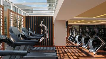 A gym with treadmills and stationary bikes, a wooden floor, and a glass ceiling.