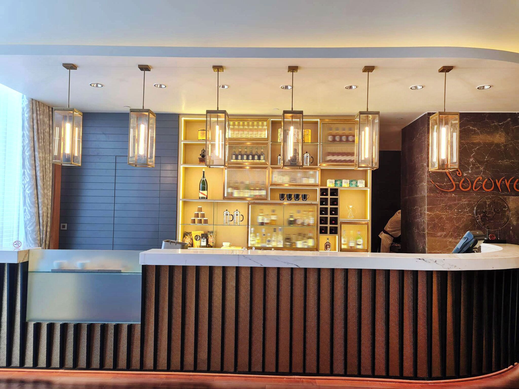 A hotel reception area with a modern design, featuring a reception desk, a wall-mounted display of various items, and pendant lighting.