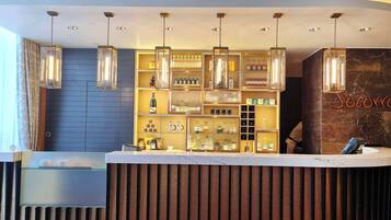 A hotel reception area with a modern design, featuring a reception desk, a wall-mounted display of various items, and pendant lighting.