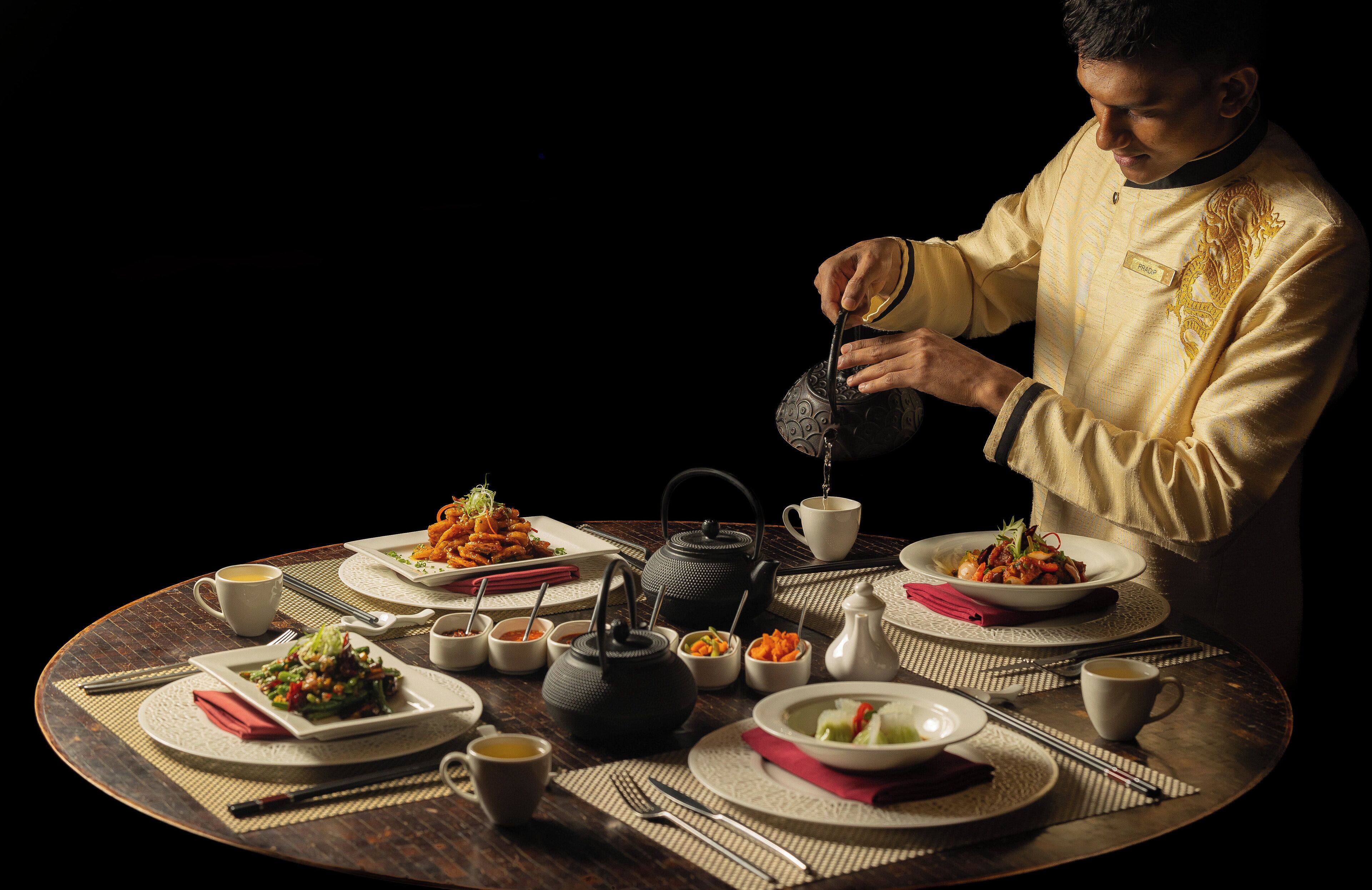 A table set for a meal with various dishes, a teapot, and a person pouring tea.