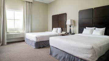 A hotel room with two beds, a window with curtains, a bedside table with a lamp, and a wall-mounted phone.