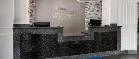 A reception desk with a Baymont Inn & Suites logo, a check-in/out sign, and a blue mat with the hotel name.
