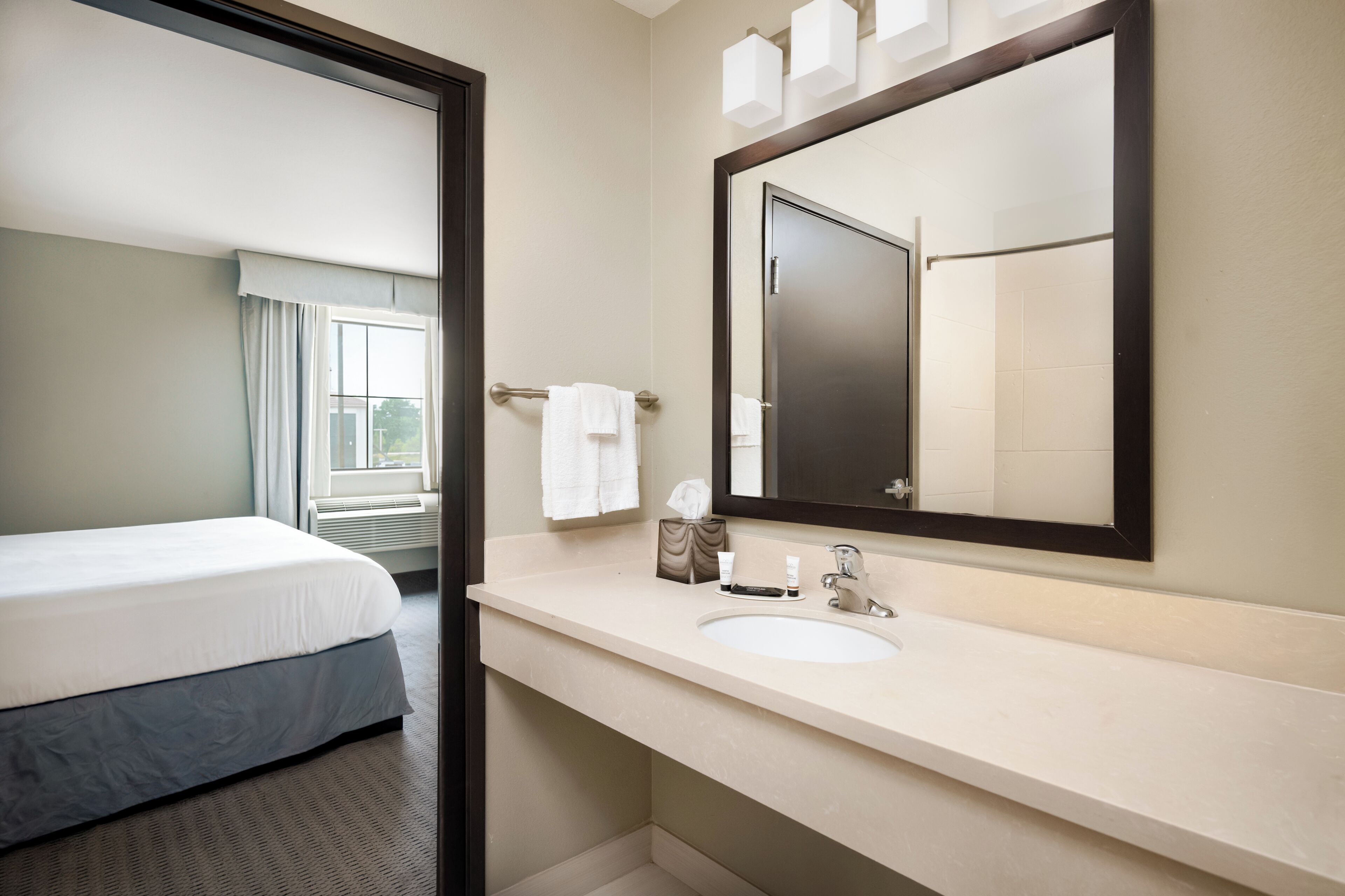 A hotel room with a bed, a bathroom with a sink, and a large mirror.