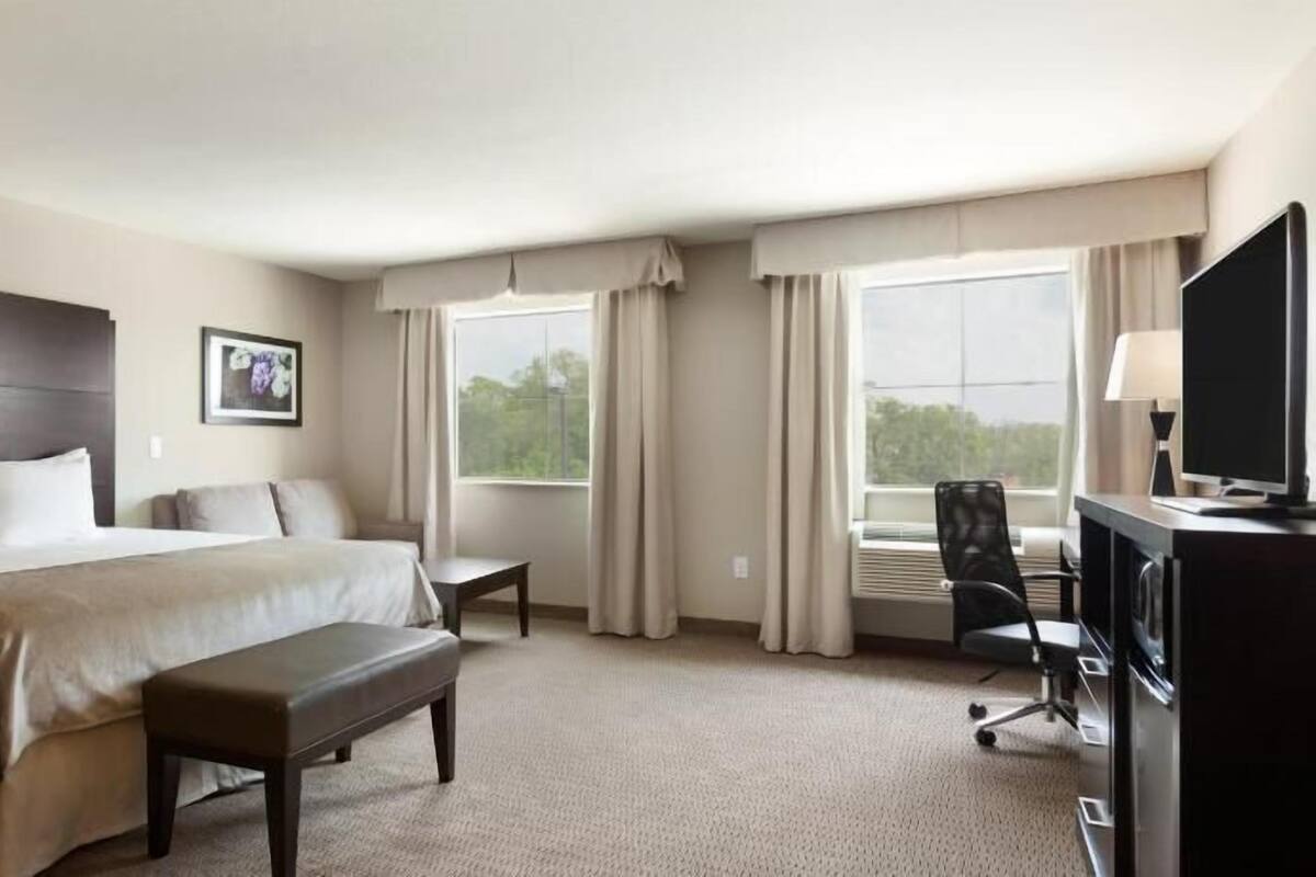 Habitación de hotel con una cama grande, un escritorio con silla, televisión y ventana con cortinas.