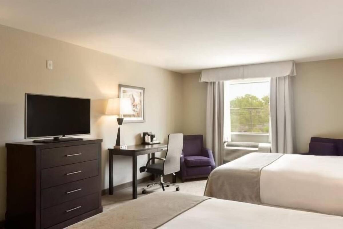 Una habitación de hotel con cama, escritorio con silla, televisor y ventana con cortinas.