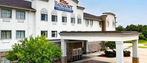 A Baymont Inn & Suites building with a covered entrance, multiple windows, and a stone facade.