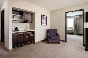 A hotel room with a kitchenette, a purple armchair, a framed picture, and a view of the hallway. - Baymont by Wyndham College Station (College Station)