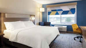 A hotel room with a large bed, a desk, a chair, a window with a city view, and a wall with geometric patterns. - Holiday Inn Express & Suites Charlotte North by IHG (Charlotte)