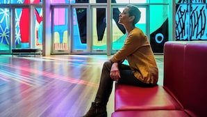 A person sitting on a red bench in a brightly lit indoor space with colorful abstract wall art. - Holiday Inn Express & Suites Charlotte North by IHG (Charlotte)