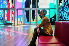 Een persoon zit op een rode bank in een helder verlichte binnenruimte met kleurrijke abstracte muurkunst.