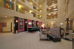 Eine mehrstöckige Hotelhalle mit Barbereich, Sitzgelegenheiten und einer Treppe.