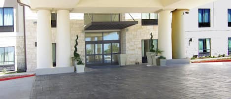 Una entrada moderna a un edificio con un vestíbulo cubierto, columnas de piedra y plantas en macetas.