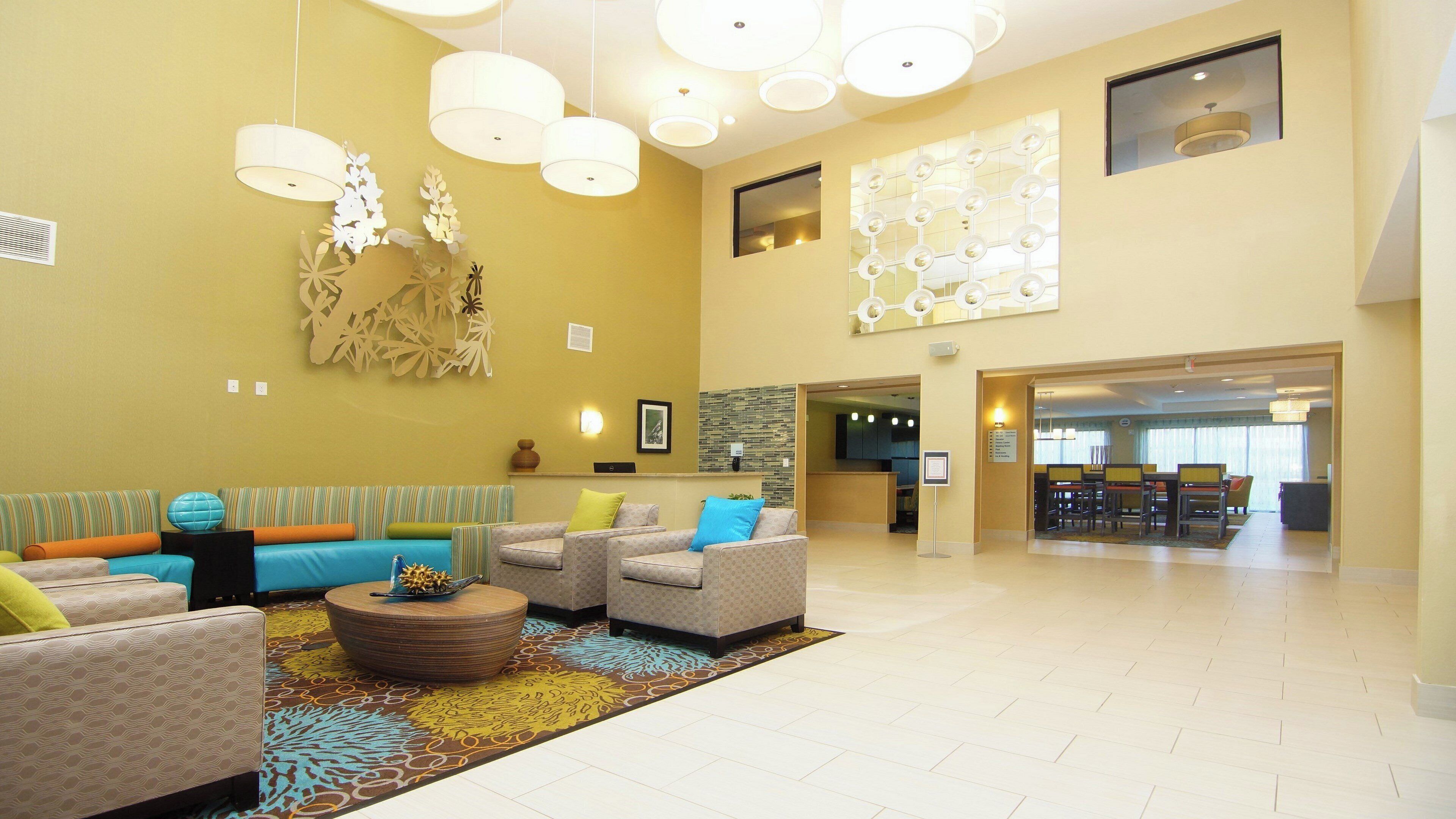 A spacious lobby with a reception desk, seating area with sofas and armchairs, and a dining area in the background.