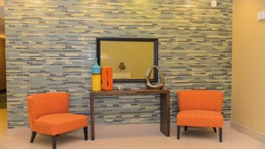 A room with two orange patterned chairs, a small table with decorative items, and a wall with a mosaic tile pattern.