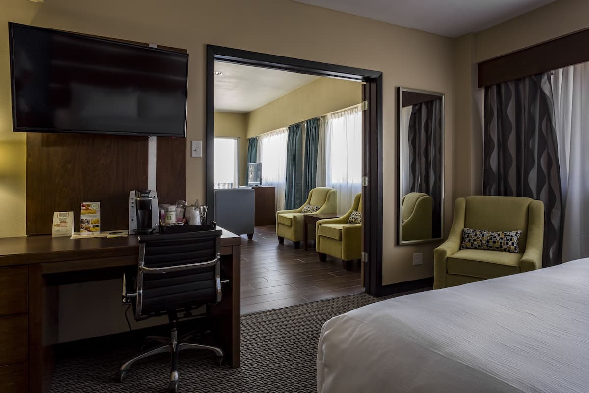 A hotel room with a bed, a desk with a chair, a television, and two armchairs.