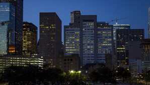 A cityscape at dusk with high-rise buildings, including a distinctive red structure on the left and a construction crane on the right.