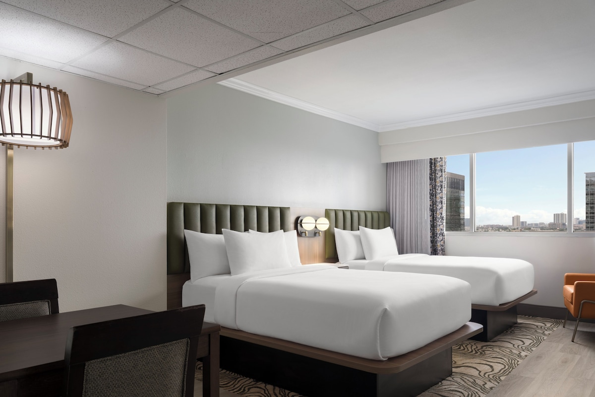 A hotel room with two beds, a desk, and a chair.