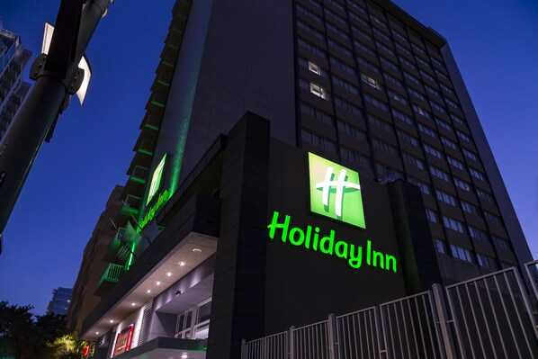 En hotellbyggnad som tillhör kedjan Holiday Inn, med en tydlig grön skylt, flera våningar och en modern arkitektonisk design.