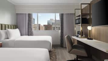 A hotel room with two beds, a desk with a chair, a flat-screen TV, and a window with curtains.