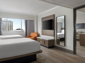 A hotel room with two beds, a TV, a desk, and a large window with a city view.