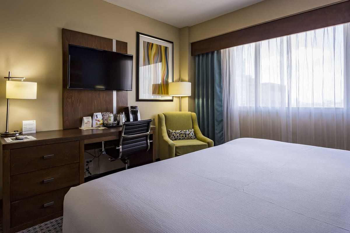 A hotel room with a large bed, a desk with a chair, a television, and a window with curtains.