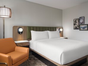 Una habitación de hotel con cama, mesita de noche, lámpara, silla y decoración en la pared.