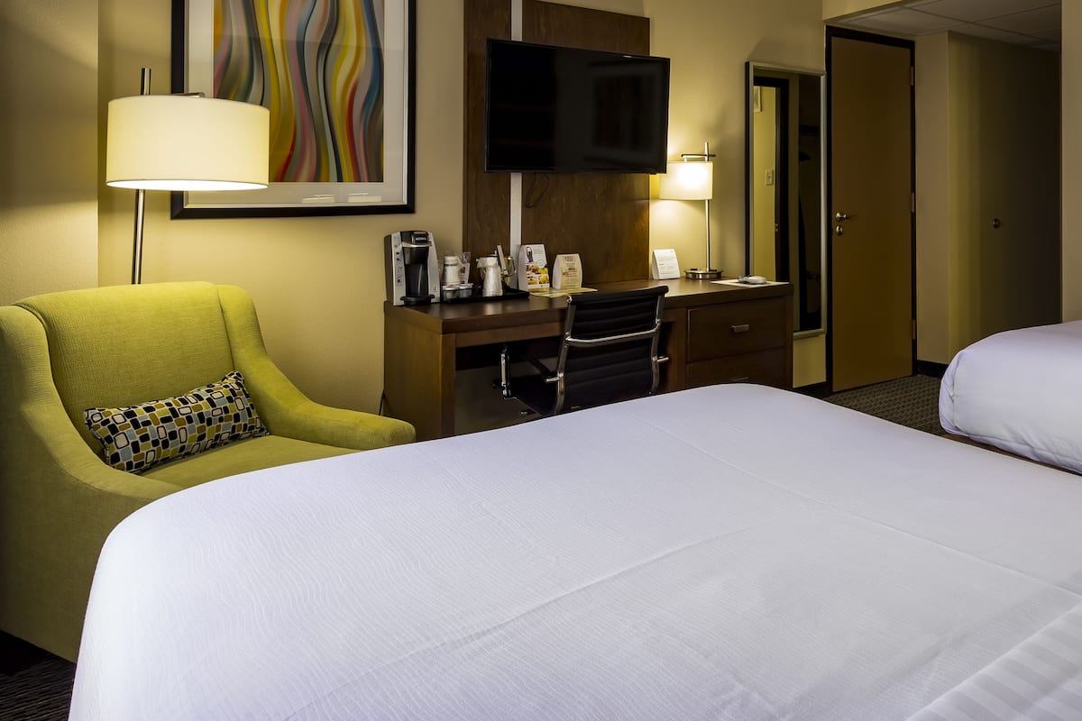 A hotel room with two beds, a desk with a computer, a chair, a TV, and a lamp.