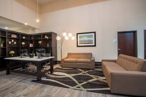Un salon moderne avec un canapé, une table basse et un bureau équipé d’ordinateurs. On y trouve également une bibliothèque avec des objets décoratifs et un tableau accroché au mur.