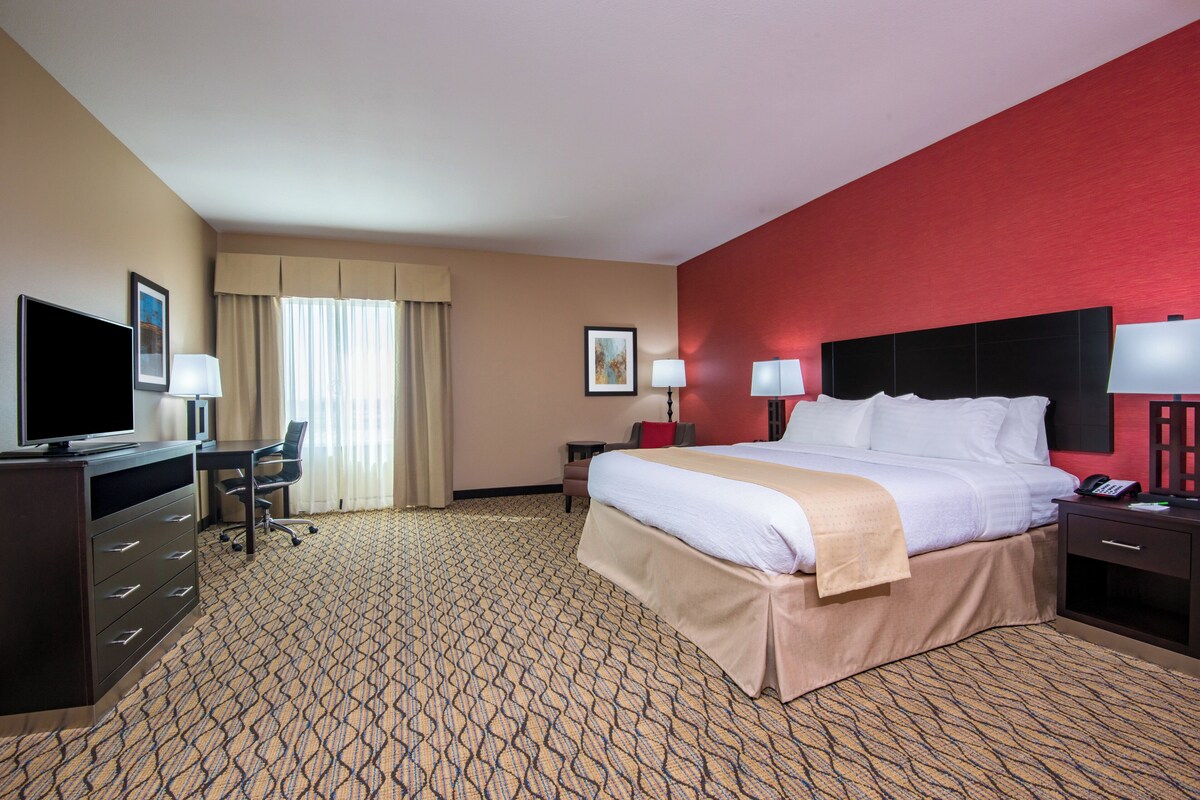 Une chambre d’hôtel avec un lit, un bureau, une télévision et un mur d’accent de couleur rouge.