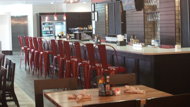 Un restaurant avec des chaises rouges, un coin bar et un écran de télévision.