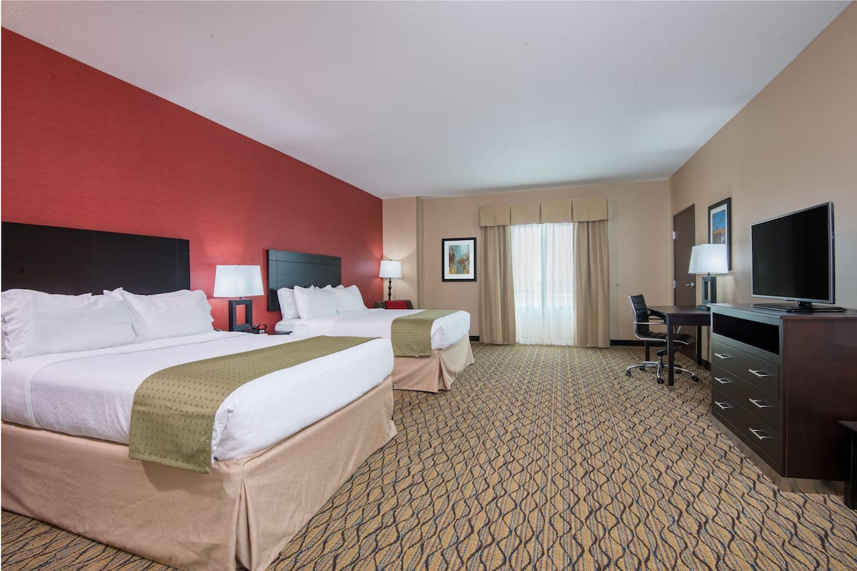 A hotel room with two beds, a desk, a television, and a chair.