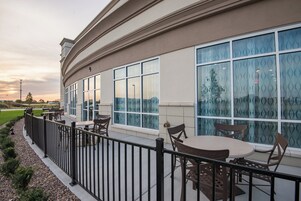 A covered outdoor seating area with tables and chairs, large windows with patterned glass, and a metal railing.